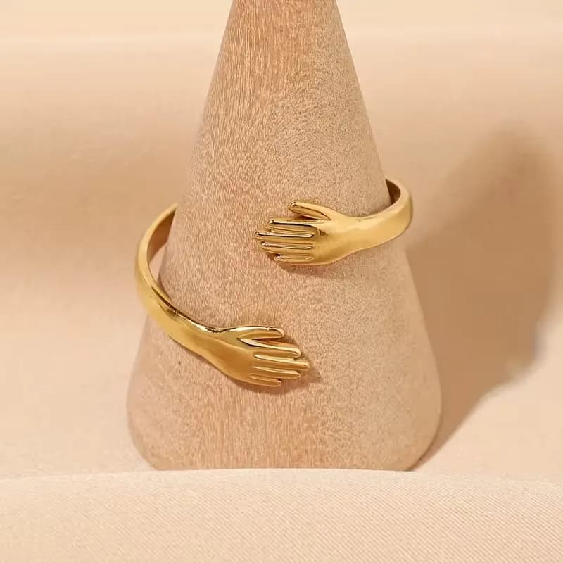 Open cuff ring in gold tone shaped as two sculpted hands meeting in a hug