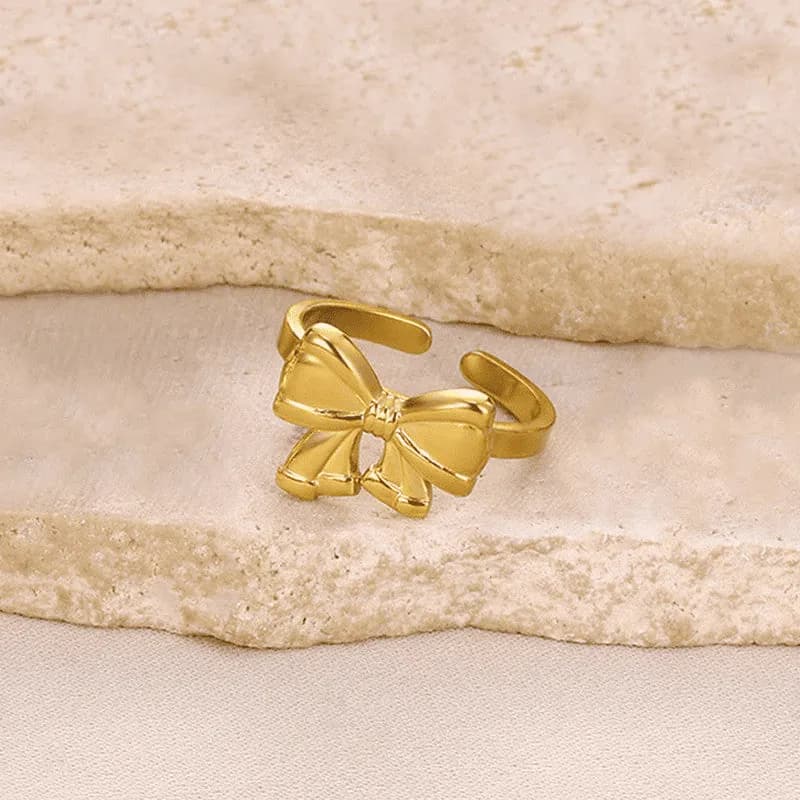 Polished gold-tone ring with a sculpted ribbon bow and an open adjustable back